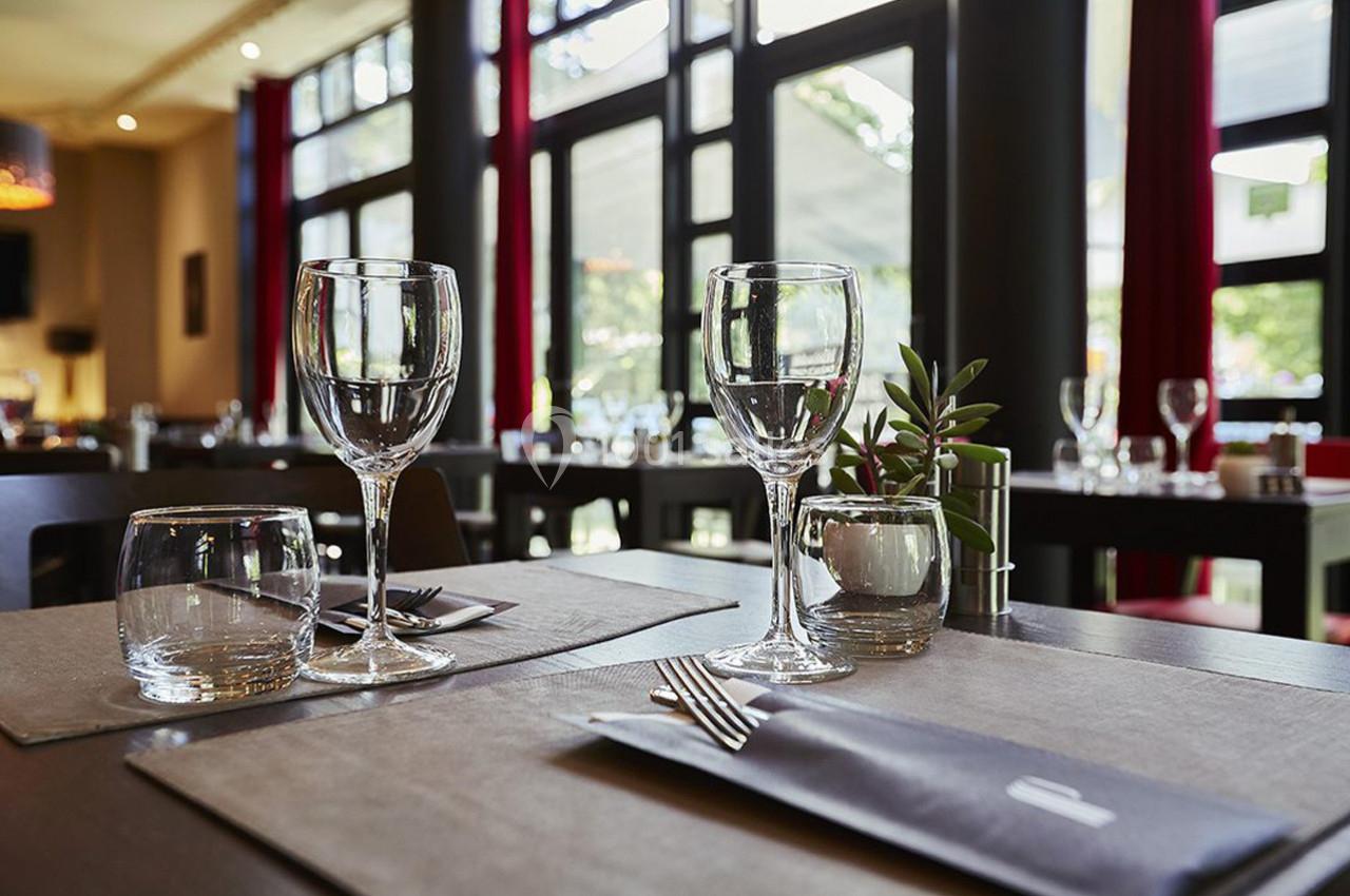 Table dressée dans un restaurant lumineux avec verres, couverts et une petite plante en décoration.