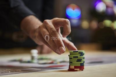 Main empilant des jetons de casino colorés sur une table, avec un arrière-plan flou de lumières et de jeux.