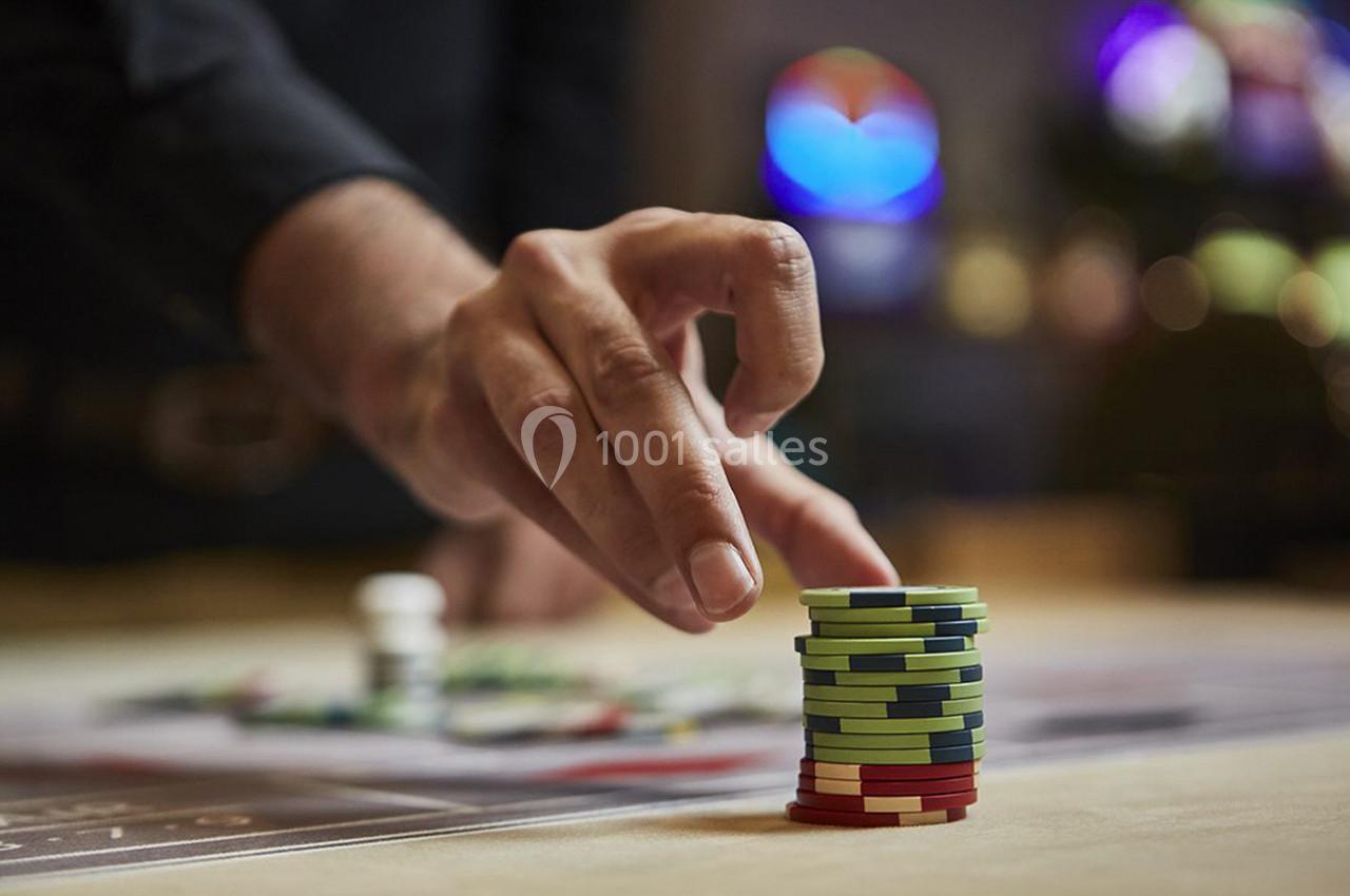 Main empilant des jetons de casino colorés sur une table, avec un arrière-plan flou de lumières et de jeux.