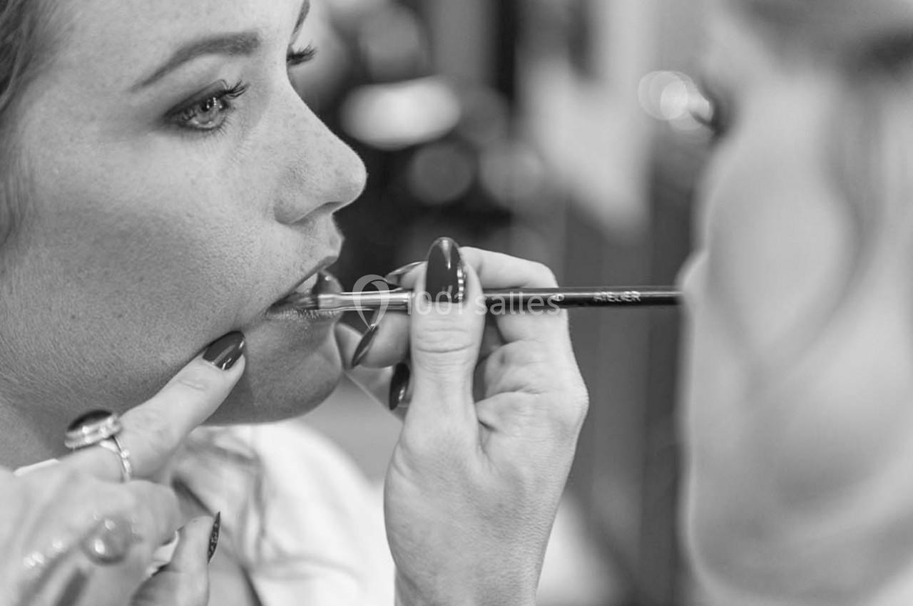 Une femme se fait maquiller les lèvres avec un pinceau dans un environnement lumineux.