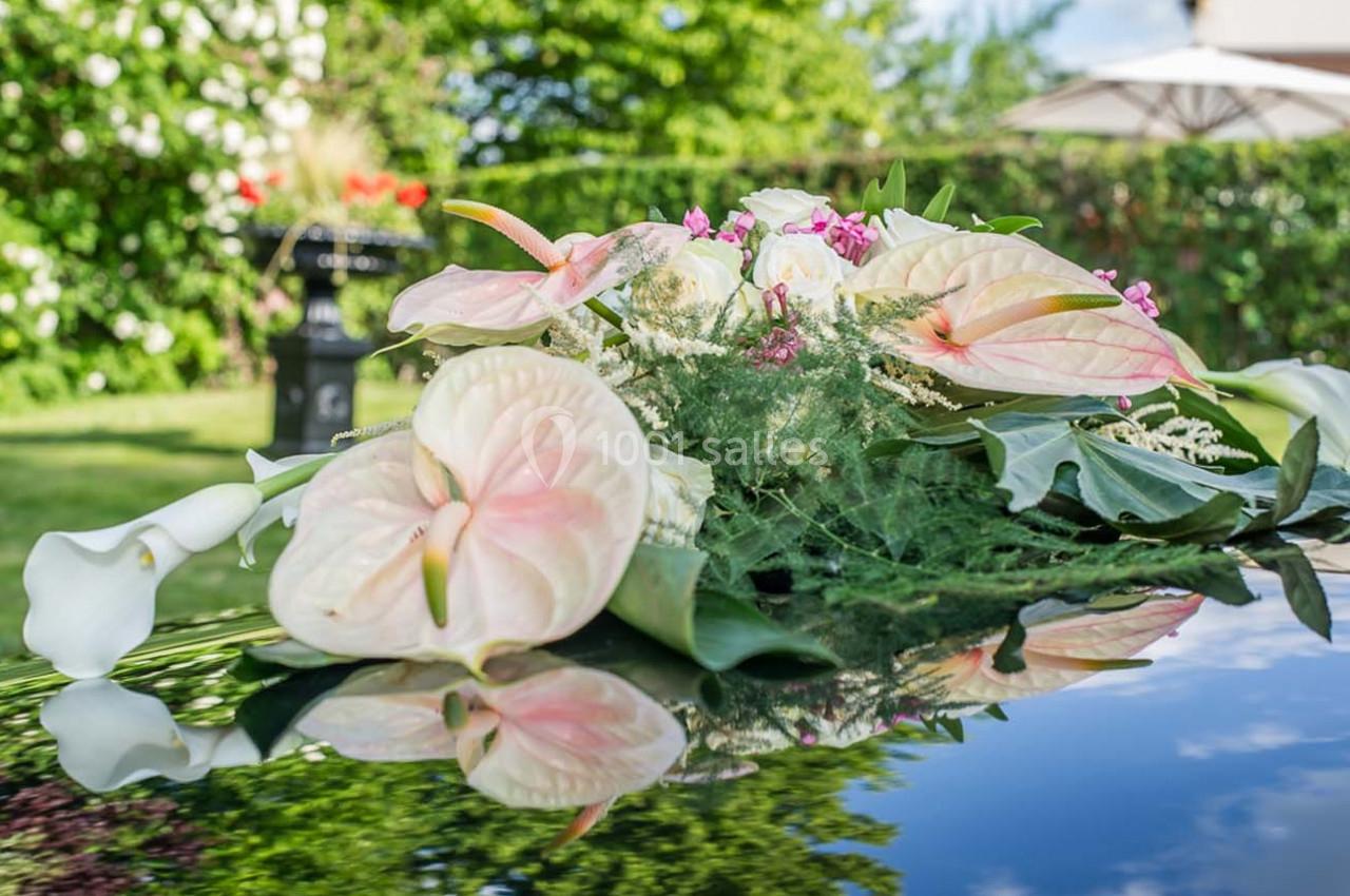 Bouquet d'anthuriums roses et de feuillages verts posé sur une surface réfléchissante dans un jardin ensoleillé.