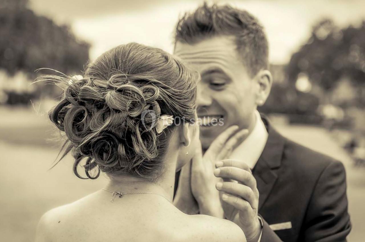 Un couple en tenue de mariage échange un moment complice dans un parc, vu de dos pour la mariée.
