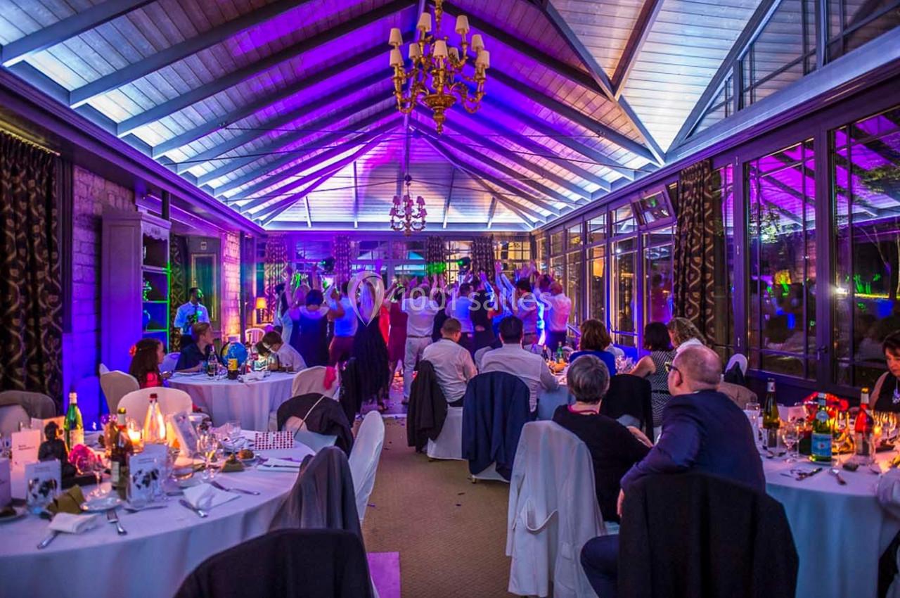Salle de réception illuminée en violet avec des invités assis à des tables et des personnes dansant au fond.
