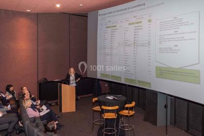 Un groupe de personnes en tenue formelle pose sur une scène lors d'un événement avec un écran affichant des logos en arrière…