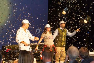 Un groupe de personnes en tenue formelle pose sur une scène lors d'un événement avec un écran affichant des logos en arrière…