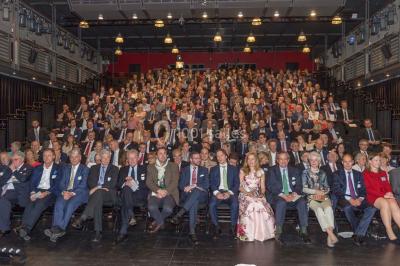 Un groupe de personnes en tenue formelle pose sur une scène lors d'un événement avec un écran affichant des logos en arrière…