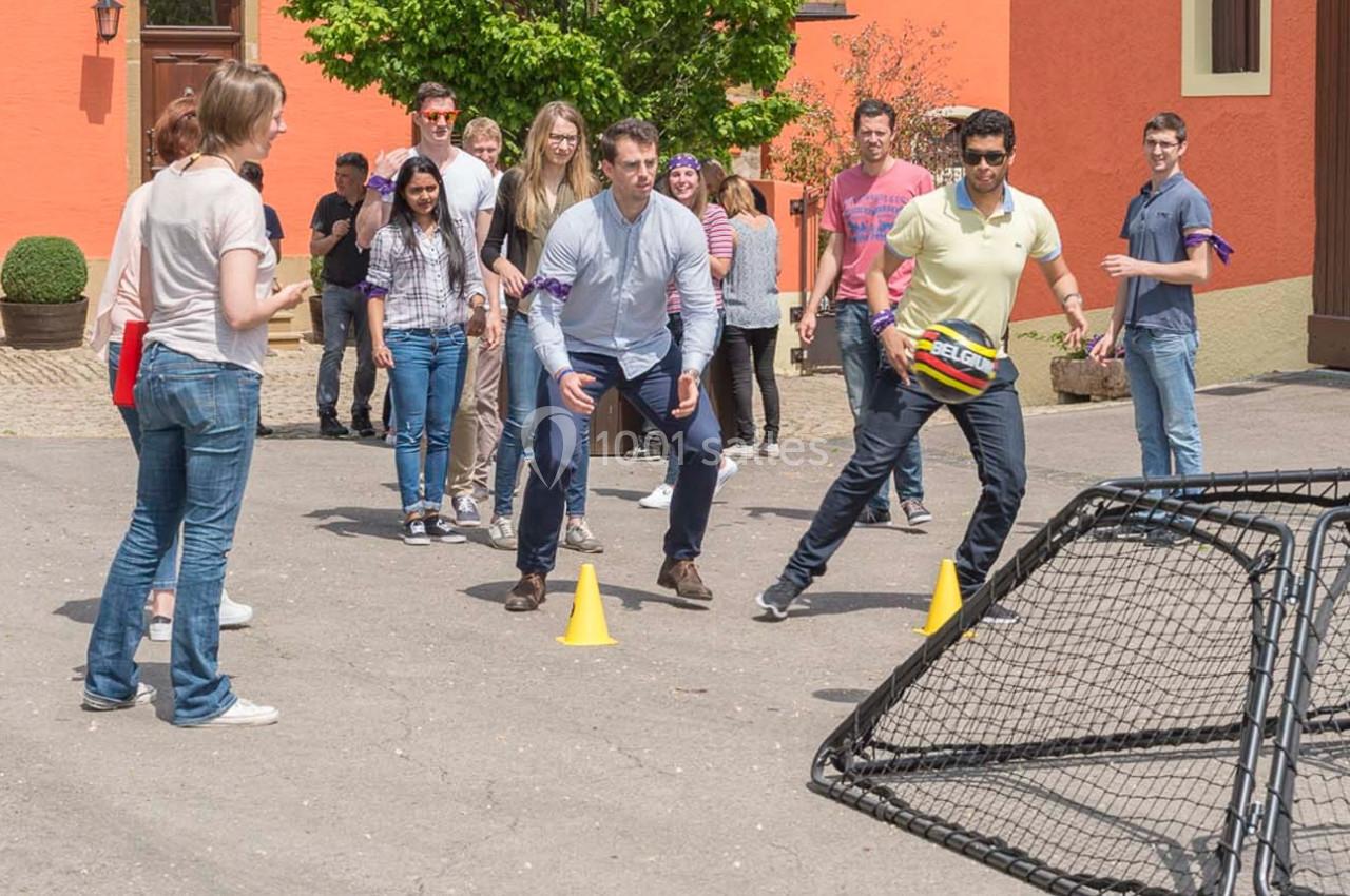 Des personnes participent à un jeu en plein air impliquant des cônes et un filet, dans une cour ensoleillée.