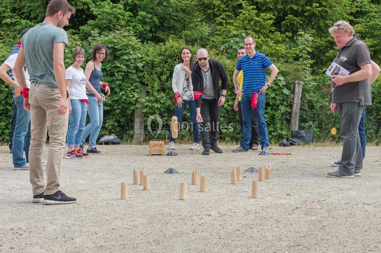 Des personnes jouent au mölkky en plein air sur un terrain en gravier, entourées de verdure.
