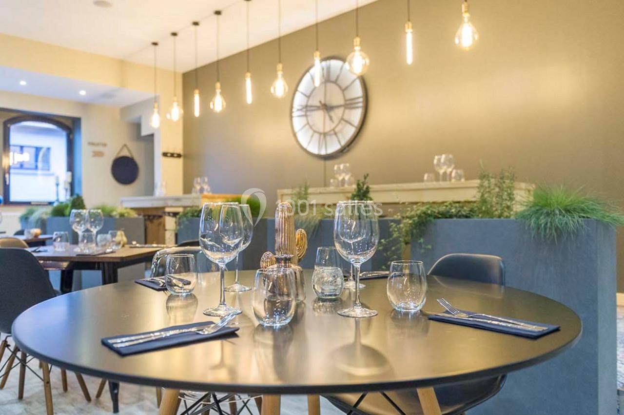 Salle de restaurant moderne avec table dressée, décorée de plantes et éclairée par des suspensions lumineuses.