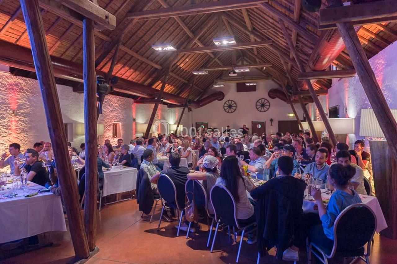 Salle de réception avec des tables dressées, occupées par de nombreux convives lors d'un événement festif.