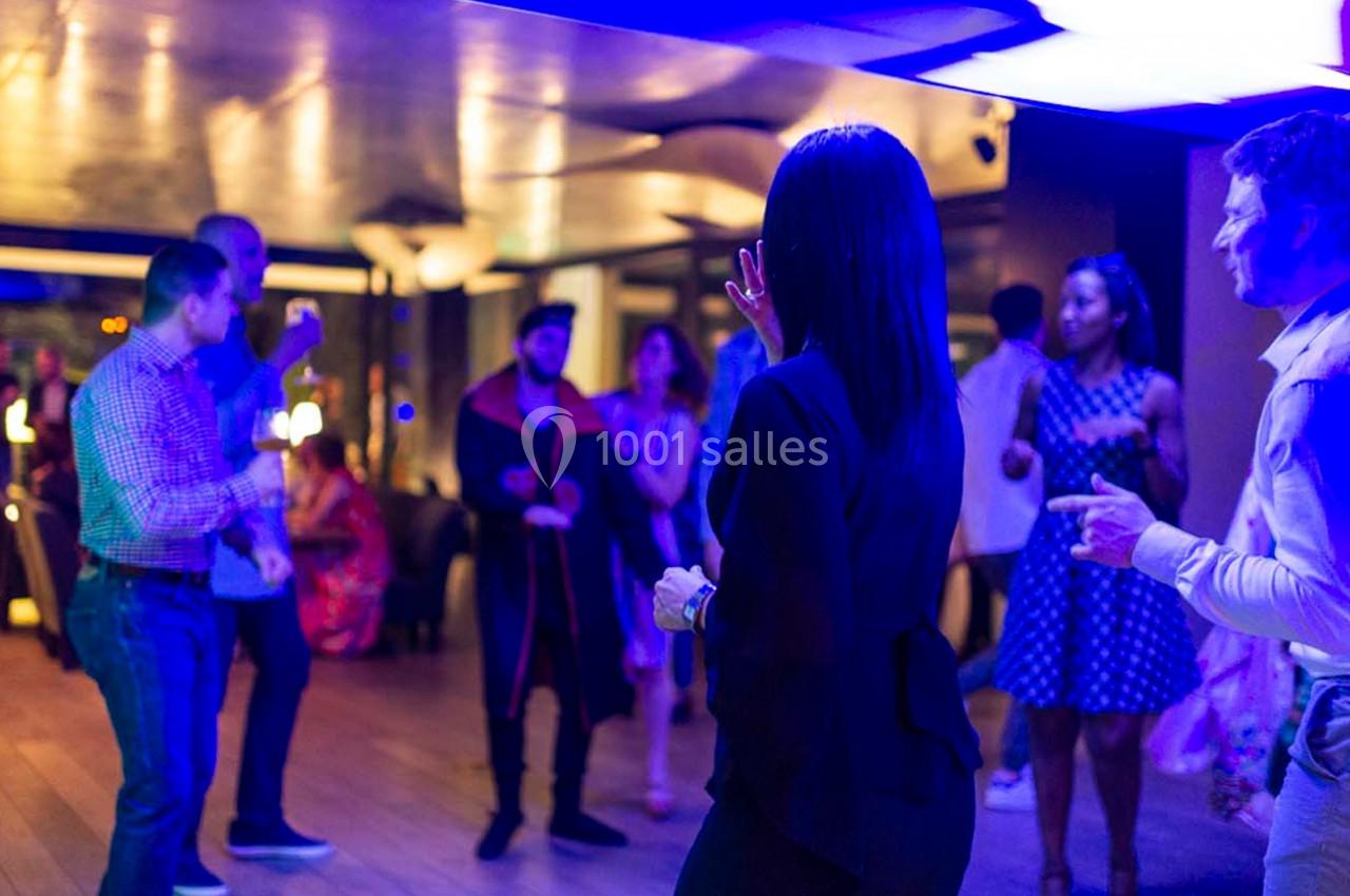 Des personnes dansent et discutent dans une salle éclairée par des lumières bleues, créant une ambiance festive.