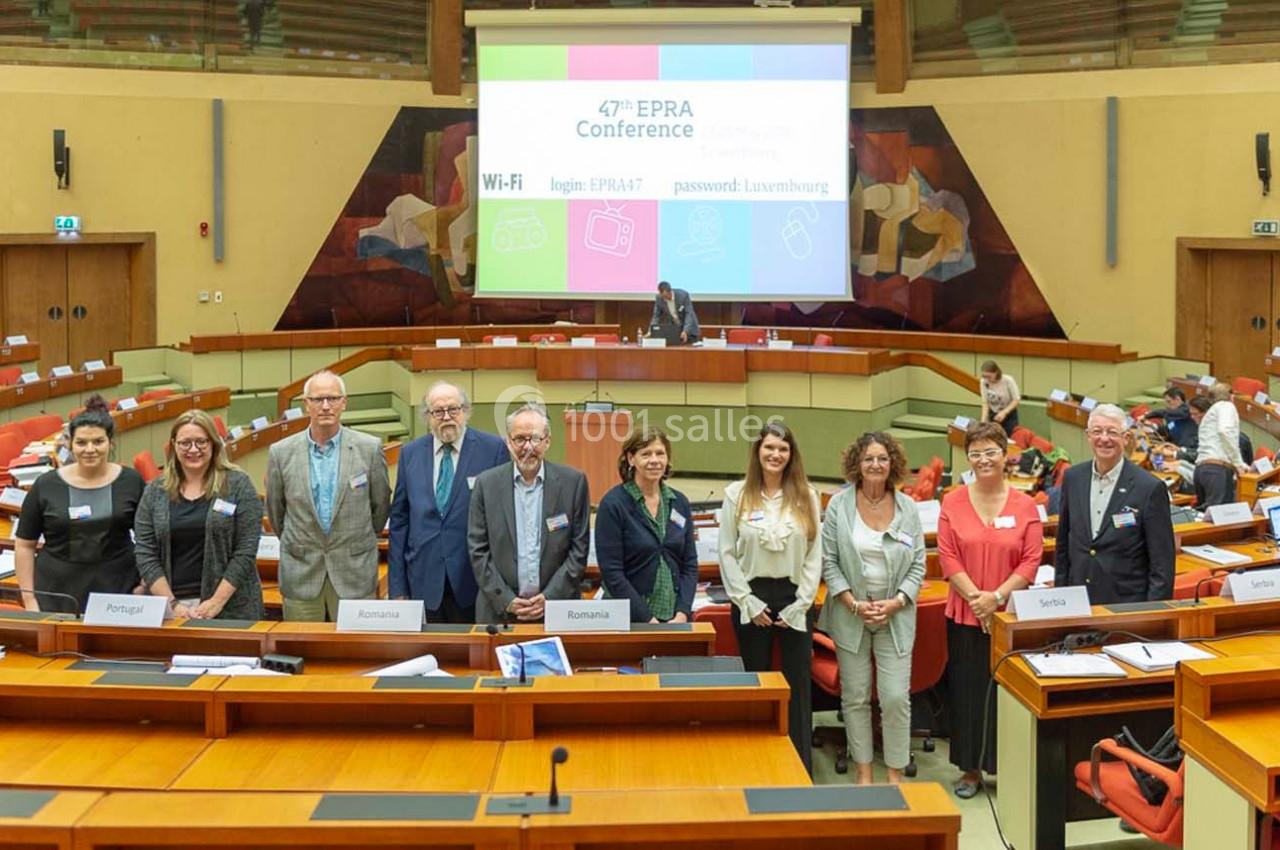 Un groupe de personnes posant devant des tables dans une salle de conférence avec un écran affichant des informations.