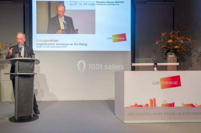 Un groupe de personnes en tenue formelle pose sur une scène lors d'un événement avec un écran affichant des logos en arrière…