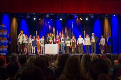 Un groupe de personnes en tenue formelle pose sur une scène lors d'un événement avec un écran affichant des logos en arrière…