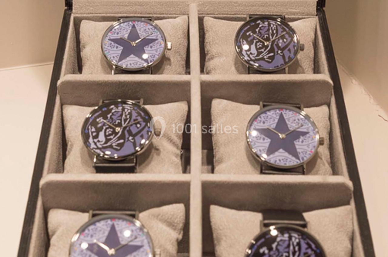 Boîte ouverte contenant six montres-bracelets avec cadrans décorés de motifs étoilés et rangées sur des coussins gris.