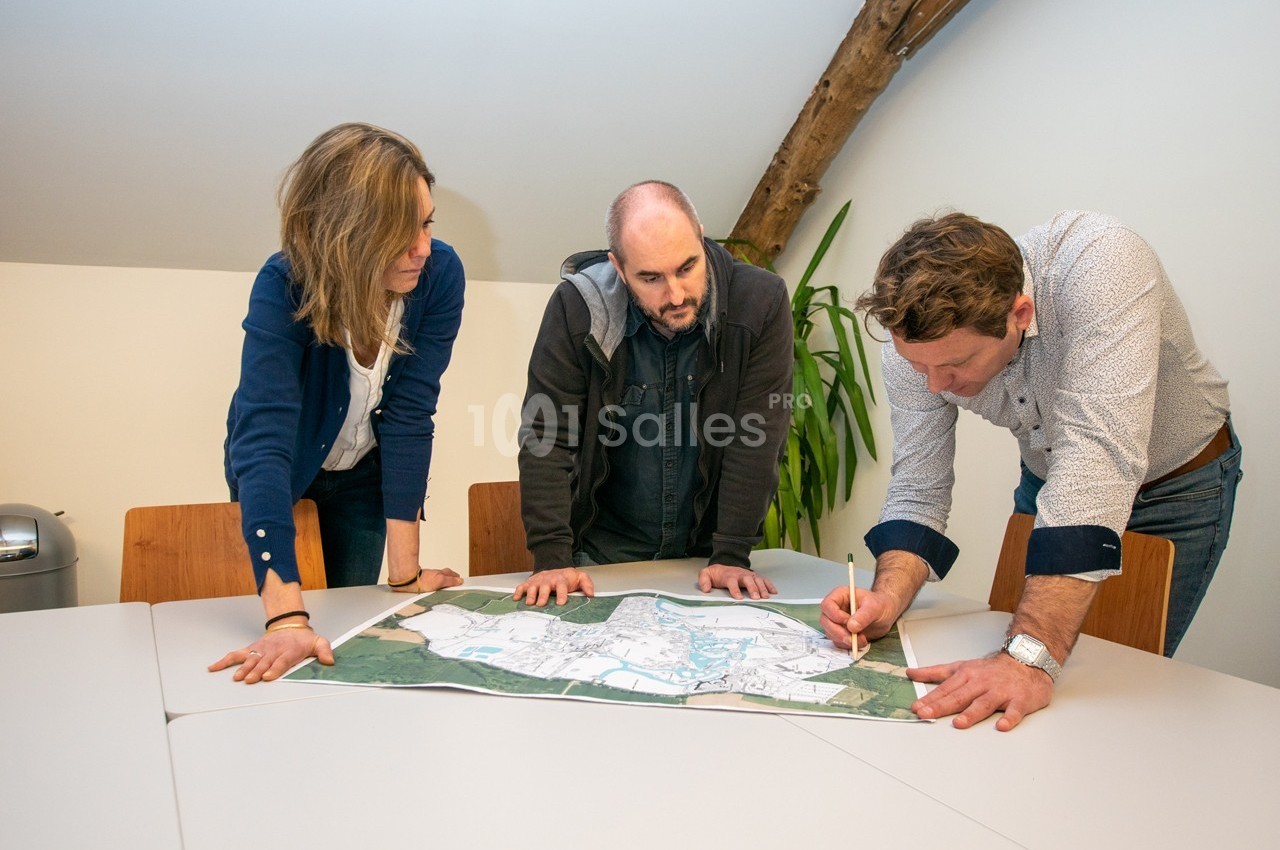 Trois personnes discutent autour d'une carte étalée sur une table dans une salle de réunion lumineuse.