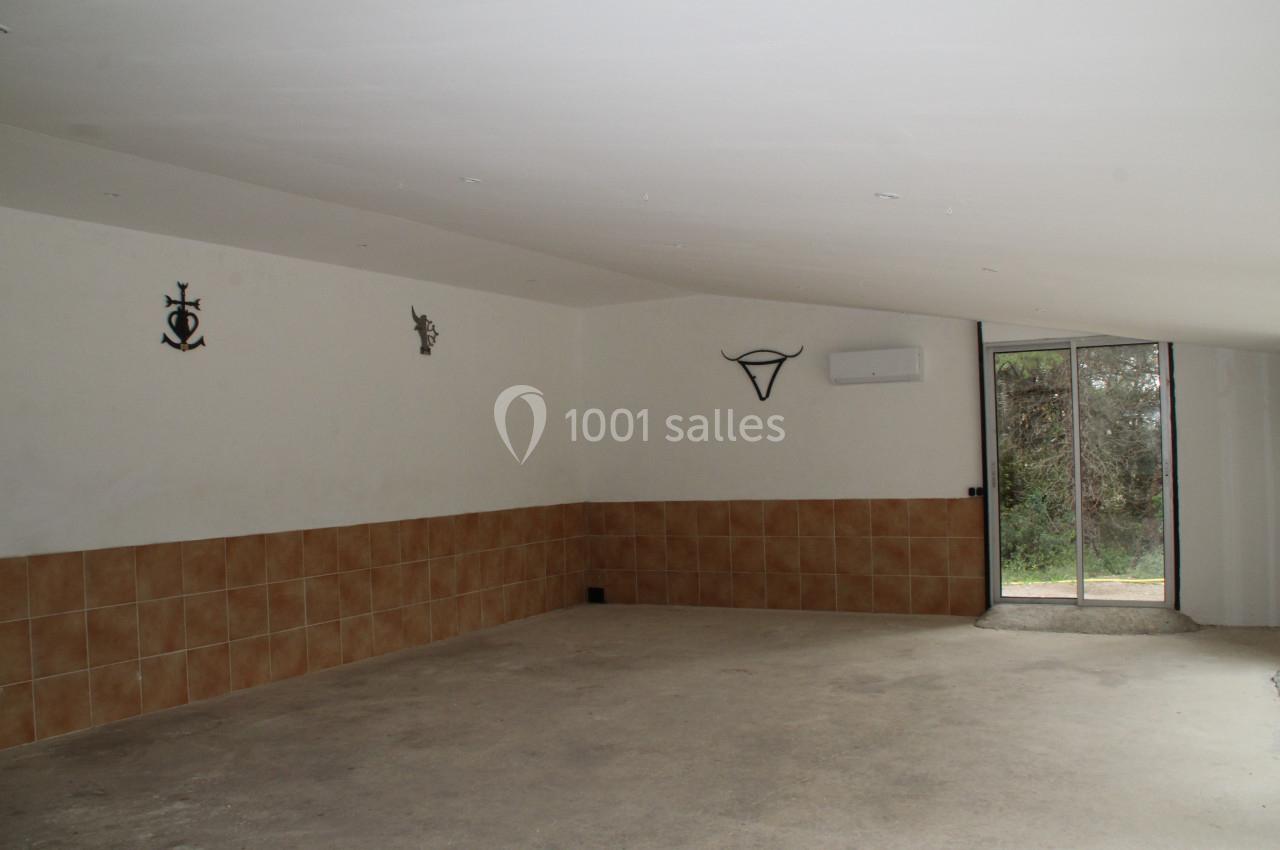 Salle vide avec sol en béton, murs partiellement carrelés, décorations murales et porte vitrée donnant sur l'extérieur.