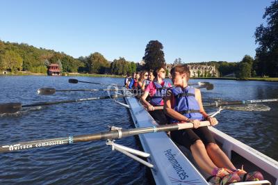 Un groupe de personnes souriantes pose dans une salle avec des rameurs et un écran projeté en arrière-plan.