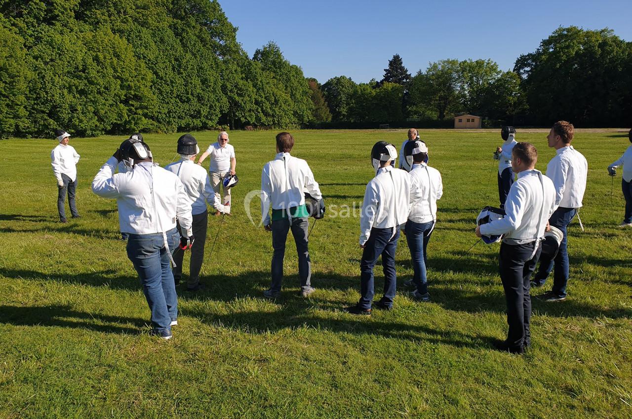 Un groupe de personnes en tenue de protection écoute un instructeur dans un champ verdoyant.