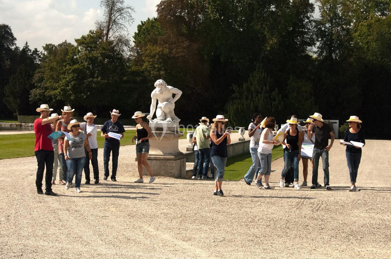 Un groupe de personnes avec des chapeaux marche et discute près d'une statue dans un parc ensoleillé.
