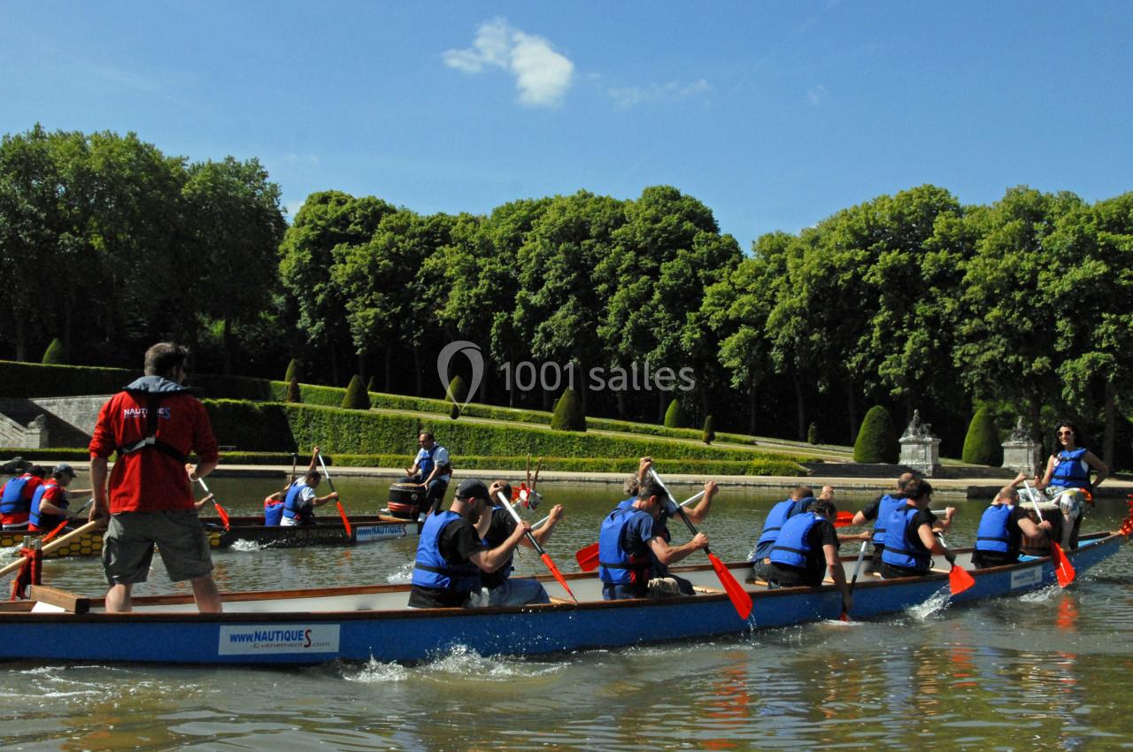 Des personnes pagayant en équipe sur des barques dans un plan d'eau entouré d'arbres et de verdure.