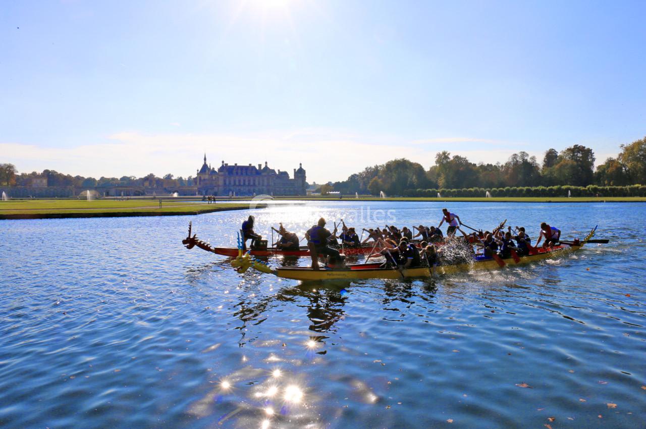 Des équipes rament sur des bateaux-dragons dans un plan d'eau, avec un château et un ciel dégagé en arrière-plan.