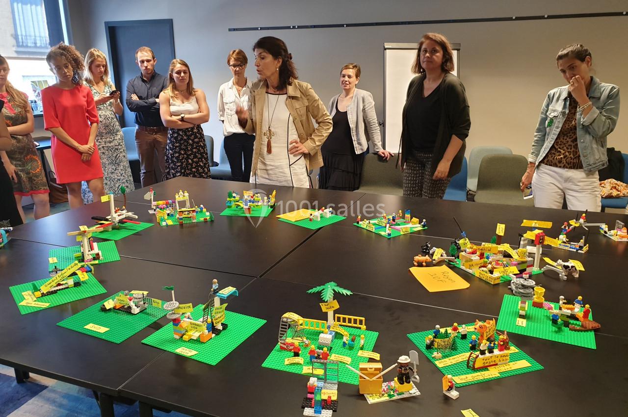 Des personnes debout autour de tables noires observant des constructions en briques Lego disposées sur celles-ci.