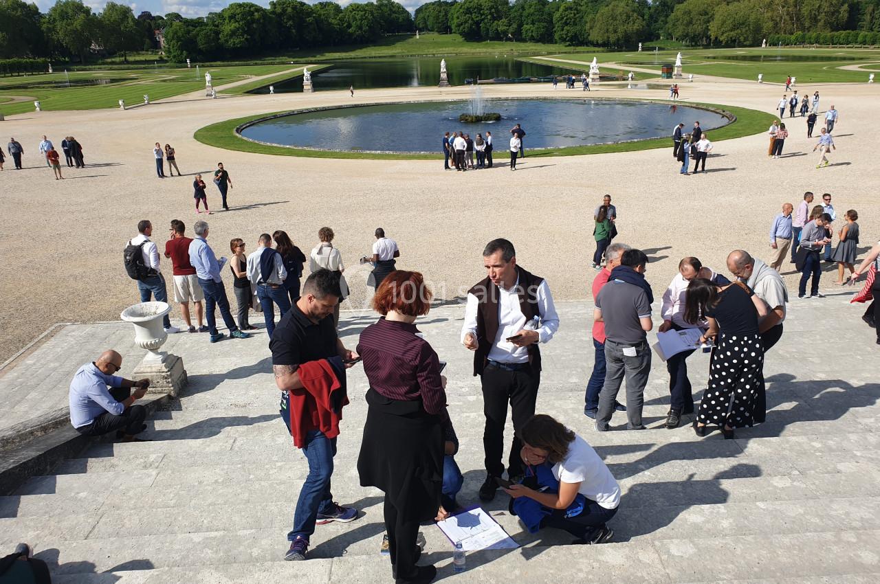 Groupe de personnes discutant et consultant des documents sur les marches d'un parc avec bassin et pelouses en arrière-plan.
