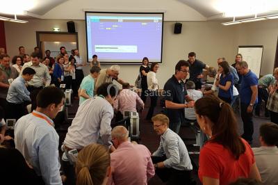 Un groupe de personnes souriantes pose dans une salle avec des rameurs et un écran projeté en arrière-plan.