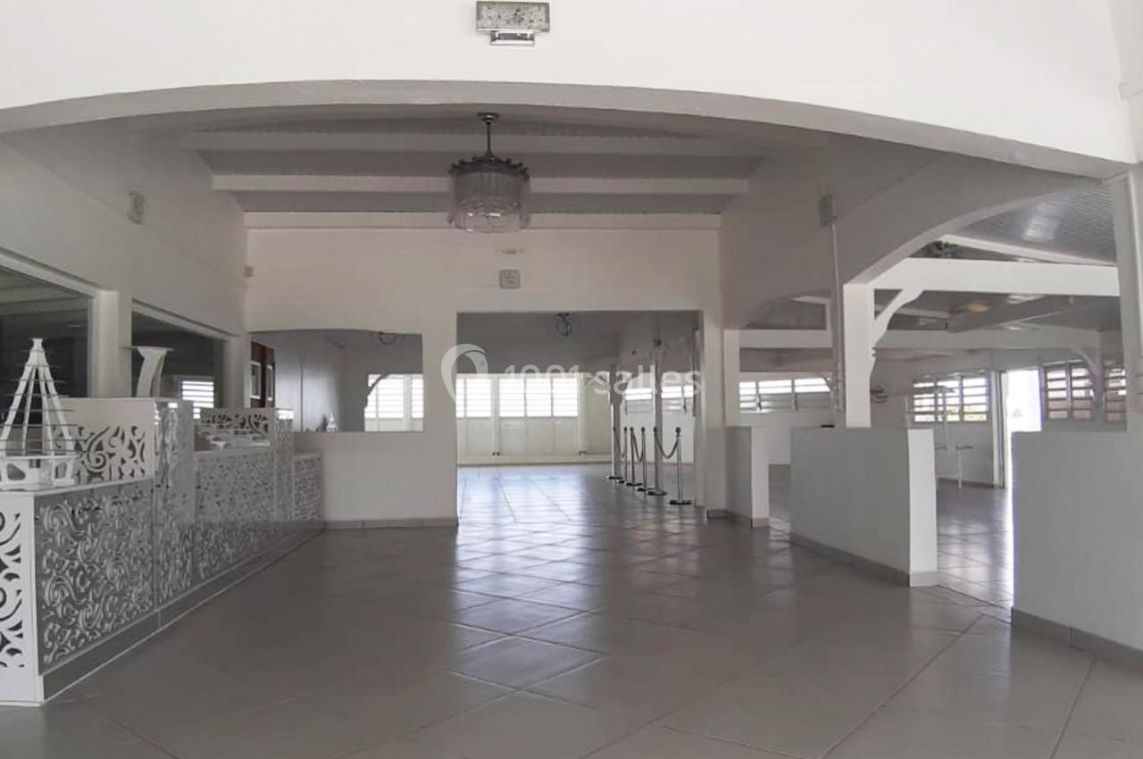 Salle spacieuse et lumineuse avec carrelage clair, poutres apparentes et décoration blanche élégante.