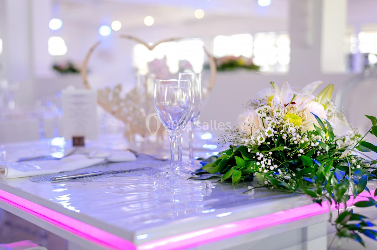 Table élégamment dressée avec bouquet de fleurs blanches, verres à pied et lumière d'ambiance rose.