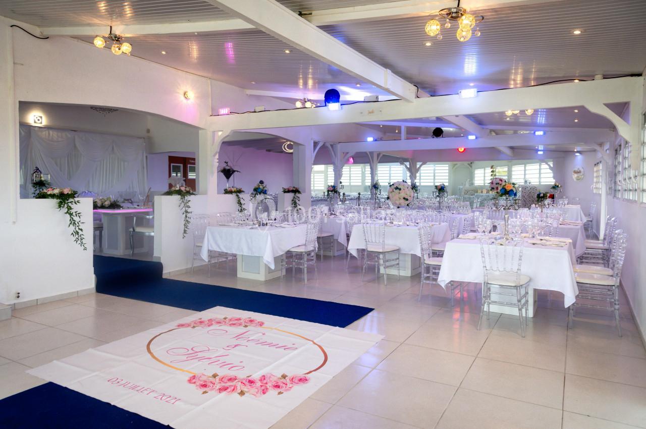 Salle de réception décorée avec des tables dressées, des chaises transparentes et un tapis personnalisé au sol.