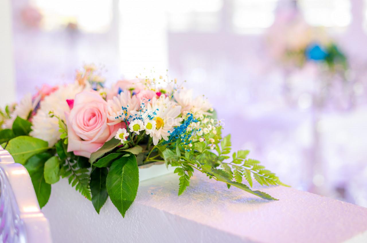 Arrangement floral avec roses roses, marguerites blanches et feuillage vert posé sur une surface blanche lumineuse.
