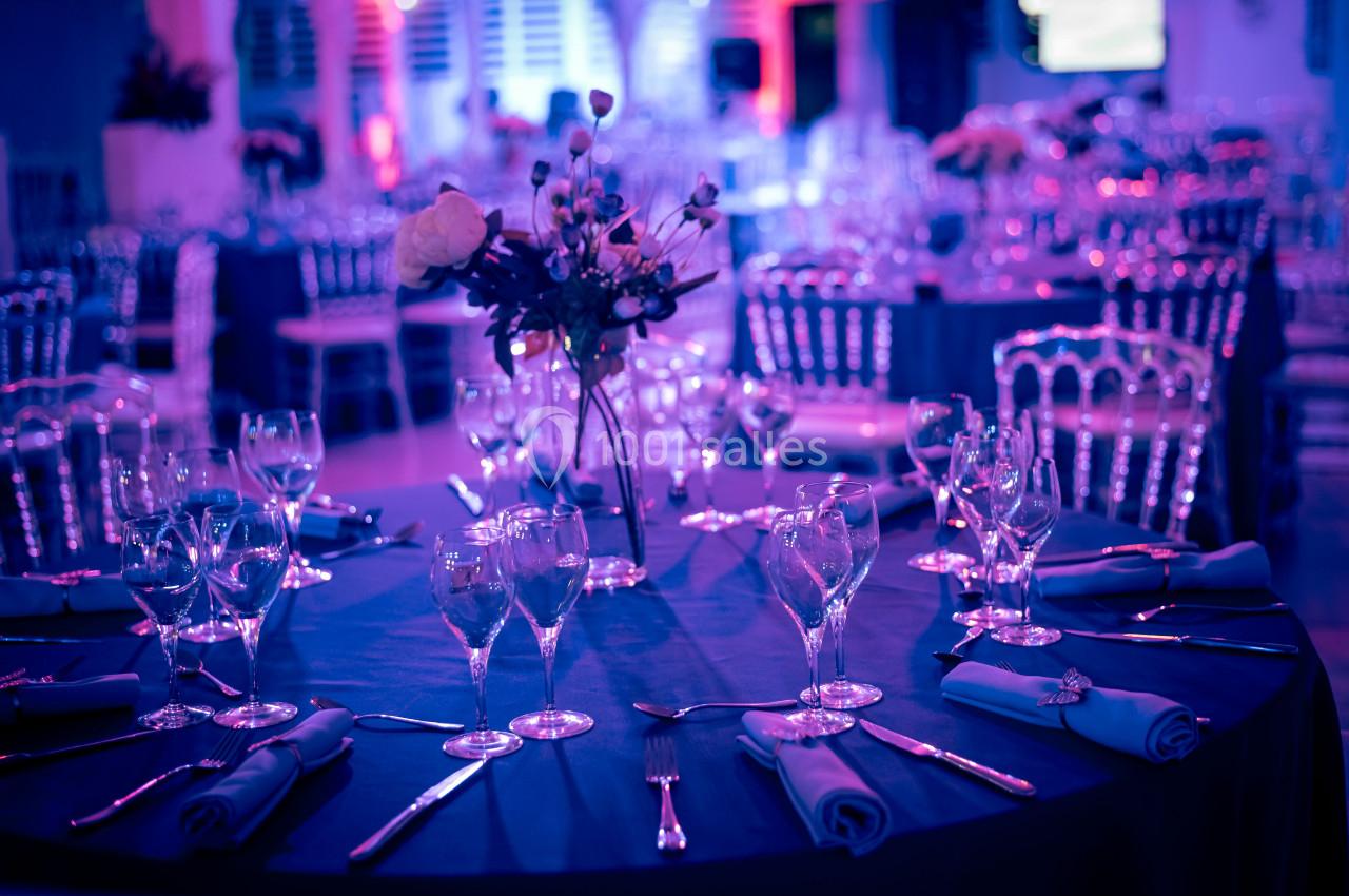 Table élégamment dressée avec nappes bleues, verres, couverts et centre de table floral dans une ambiance lumineuse tamisée.