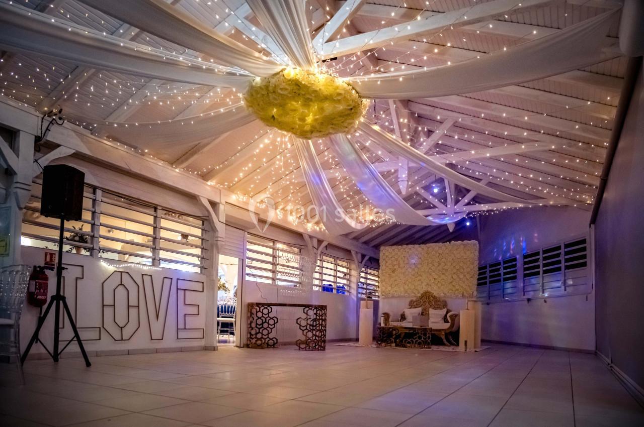 Salle décorée pour un événement, avec guirlandes lumineuses au plafond, lettres ’LOVE’ et mobilier élégant.