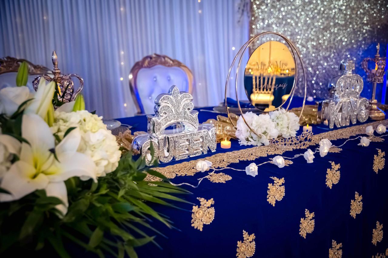 Table décorée avec des fleurs blanches, des ornements royaux ’Queen’ et ’King’, et un fond scintillant.