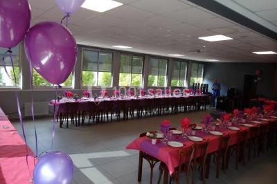 Salle de réception lumineuse avec tables dressées, nappes blanches et serviettes bleues, prête pour un événement.