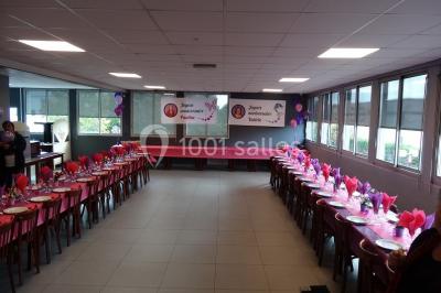 Salle de réception lumineuse avec tables dressées, nappes blanches et serviettes bleues, prête pour un événement.