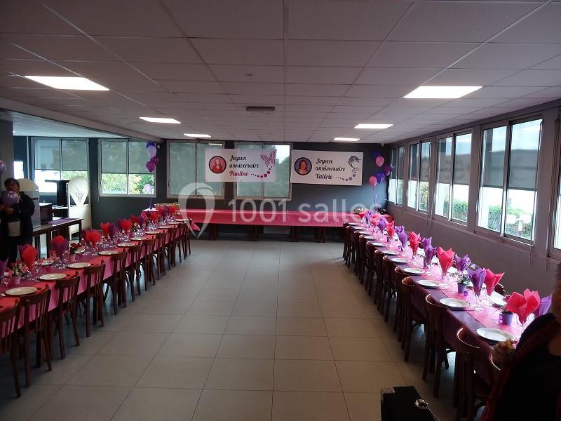 Salle décorée pour un anniversaire avec tables alignées, nappes roses, ballons et banderoles personnalisées.