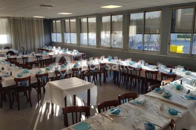 Salle de réception lumineuse avec tables dressées, nappes blanches et serviettes bleues, prête pour un événement.