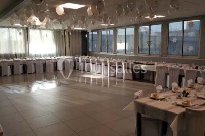 Salle de réception lumineuse avec tables dressées, nappes blanches et serviettes bleues, prête pour un événement.