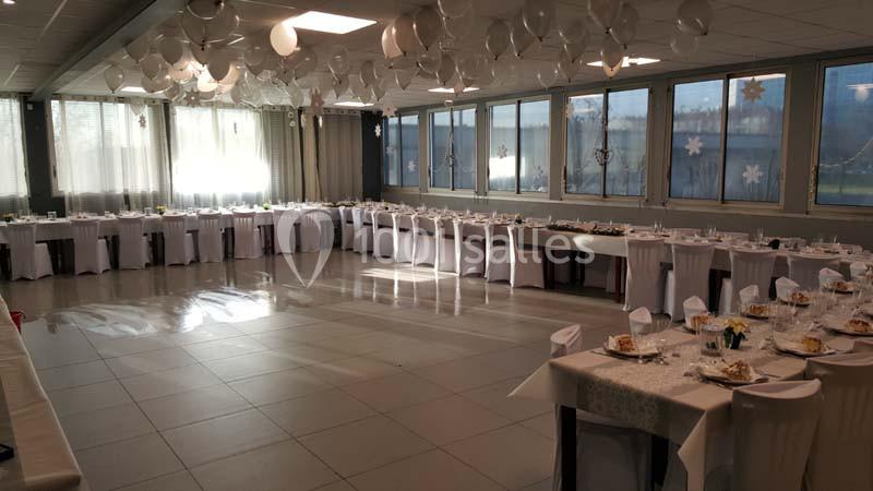 Salle de réception décorée avec des ballons blancs au plafond et des tables dressées pour un événement.