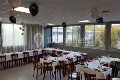 Salle de réception lumineuse avec tables dressées, nappes blanches et serviettes bleues, prête pour un événement.