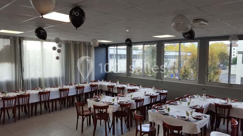 Salle décorée pour un 50e anniversaire, avec des tables dressées et des ballons noirs et blancs suspendus.