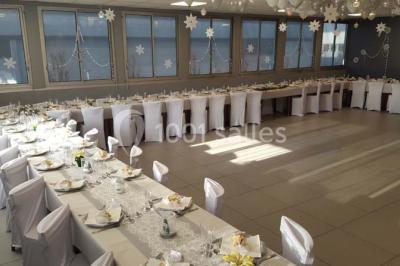 Salle de réception lumineuse avec tables dressées, nappes blanches et serviettes bleues, prête pour un événement.