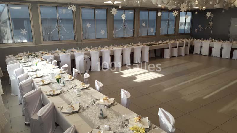 Salle décorée pour un événement, avec de longues tables dressées, nappes blanches et décorations hivernales.