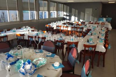 Salle de réception lumineuse avec tables dressées, nappes blanches et serviettes bleues, prête pour un événement.