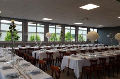 Salle de réception lumineuse avec tables dressées, nappes blanches et serviettes bleues, prête pour un événement.