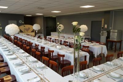 Salle de réception lumineuse avec tables dressées, nappes blanches et serviettes bleues, prête pour un événement.