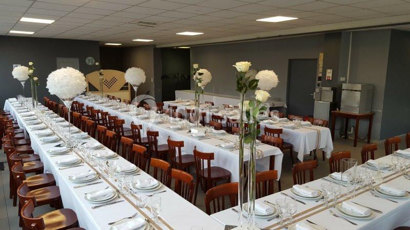 Salle de réception avec de longues tables dressées, nappes blanches, vaisselle élégante et décorations florales.